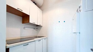 Una cocina compacta con armarios blancos, un lavamanos de acero inoxidable y un refrigerador blanco.