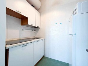 Une cuisine de taille réduite avec des meubles blancs, un évier en acier inoxydable et un réfrigérateur blanc.