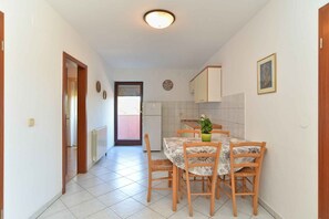 Um corredor estreito que leva a uma área de jantar com mesa e cadeiras, um radiador e uma porta.