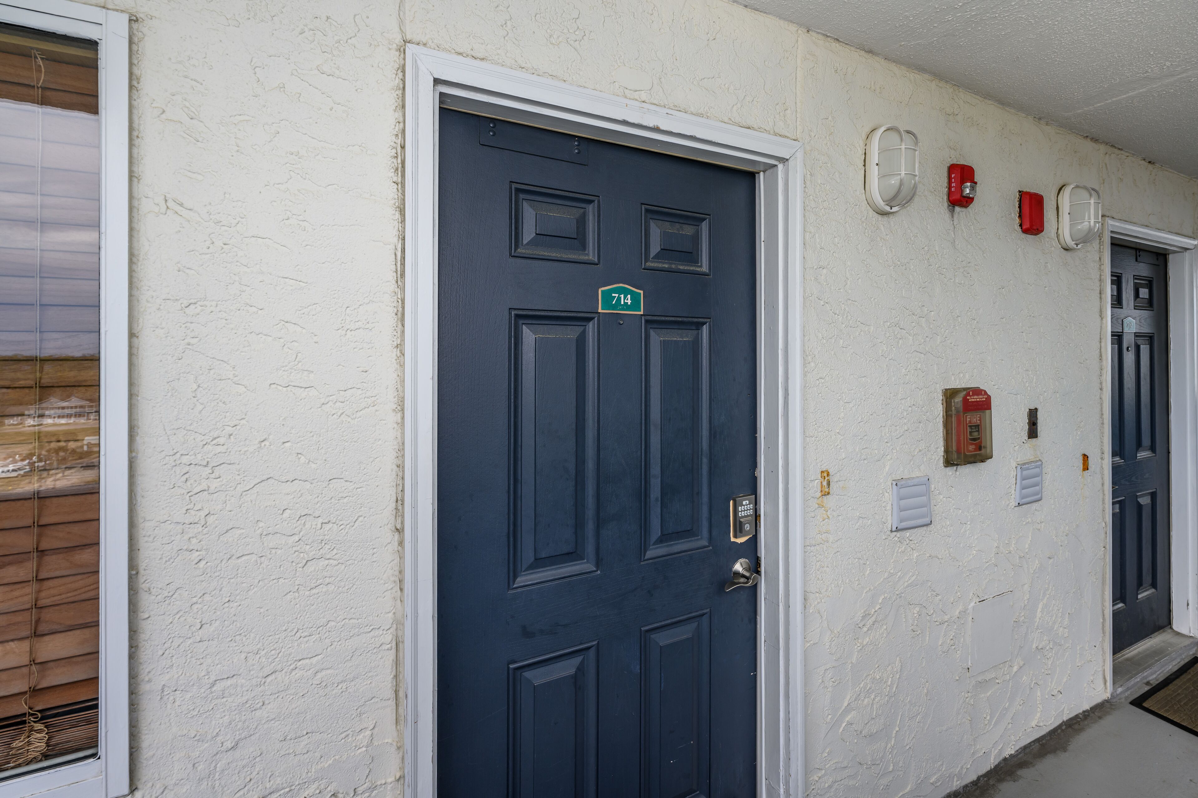 A dark blue door with a number plate, white textured walls, and fire safety equipment.