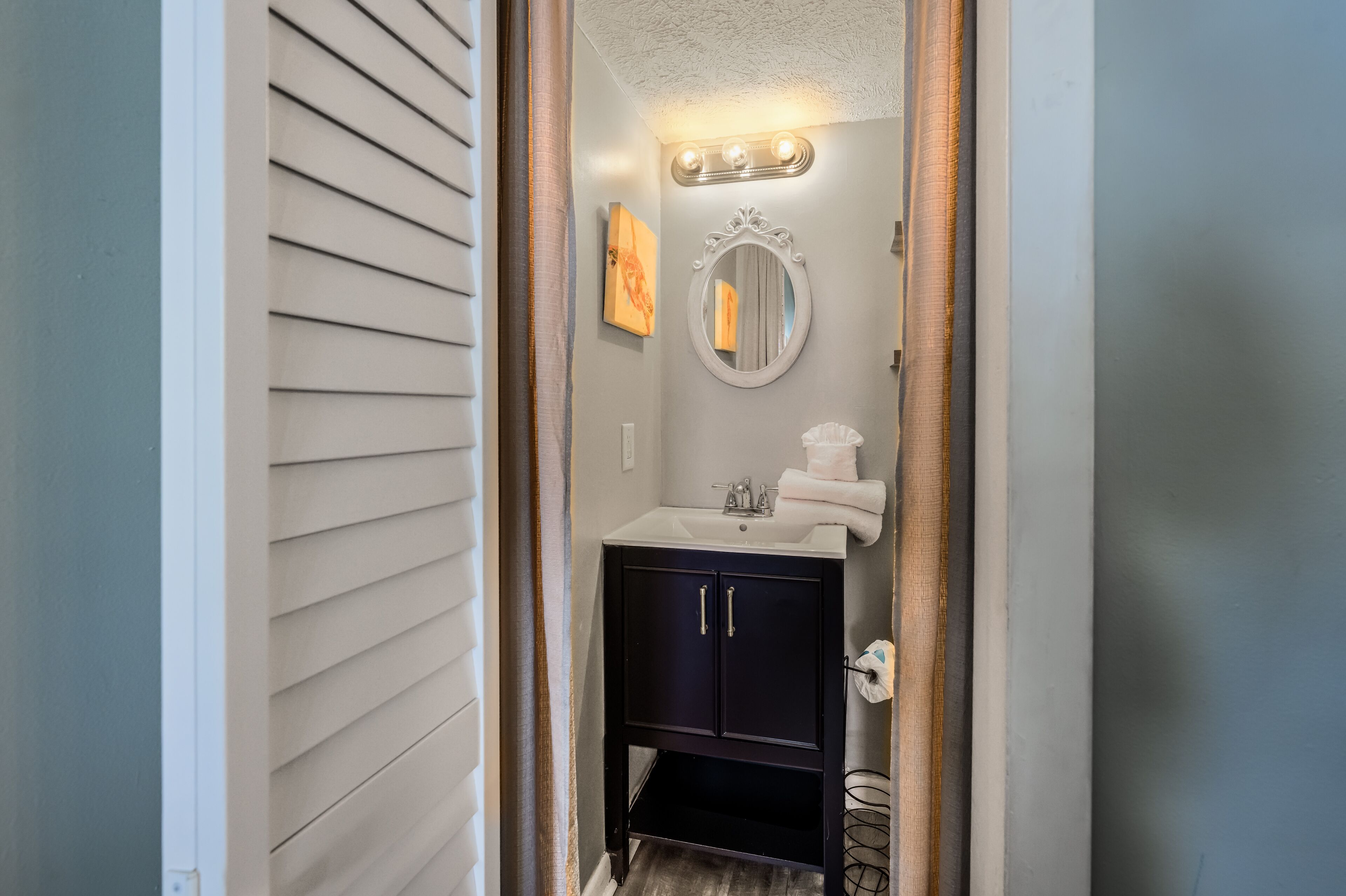 A bathroom with a white sink, dark cabinets, a mirror, and a towel rack.