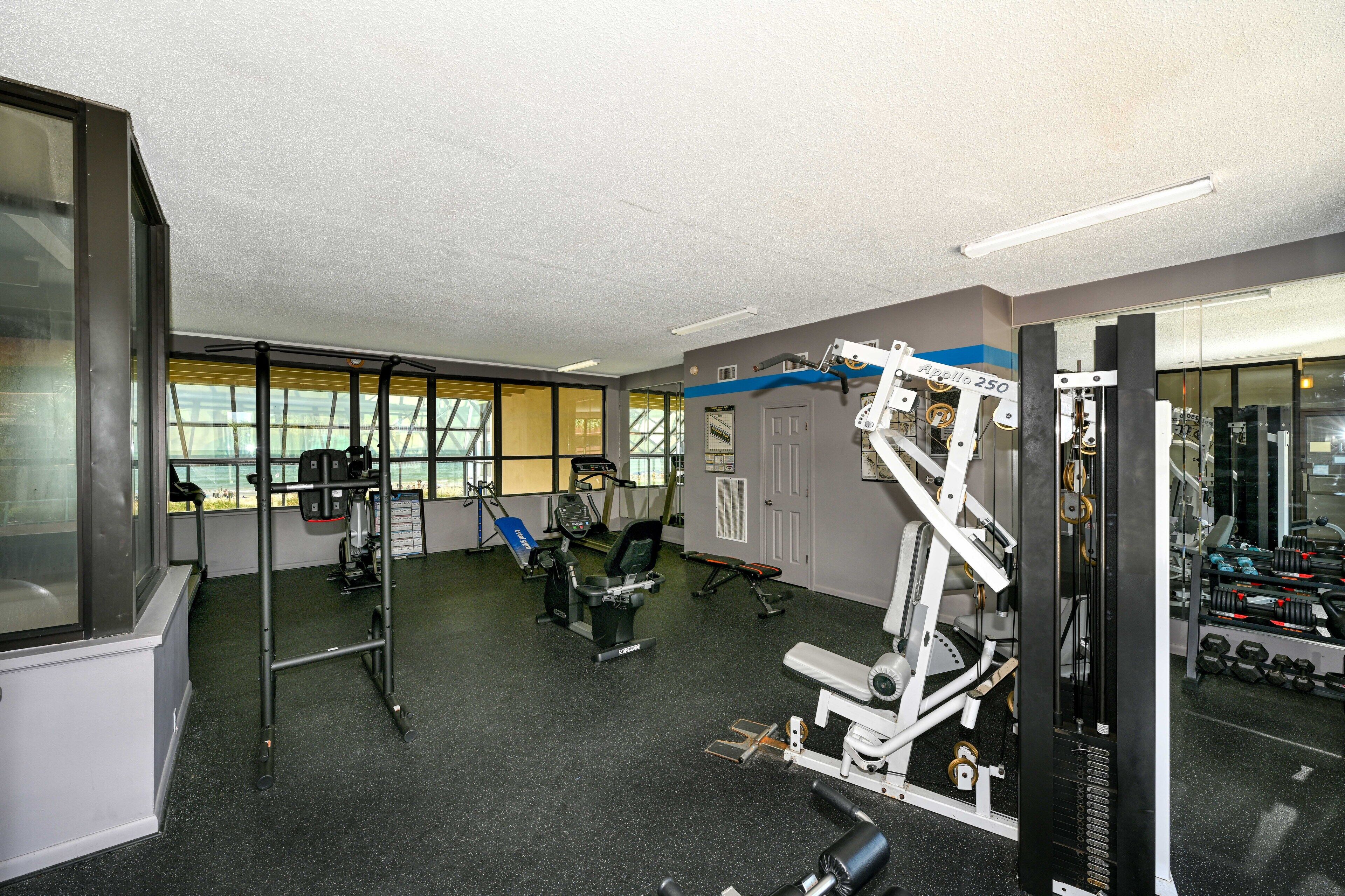 Un gimnasio con diversos equipos de ejercicio, ventanas amplias y vistas al exterior.