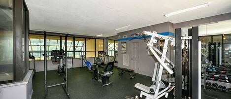 Un gimnasio con diversos equipos de ejercicio, ventanas amplias y vistas al exterior.