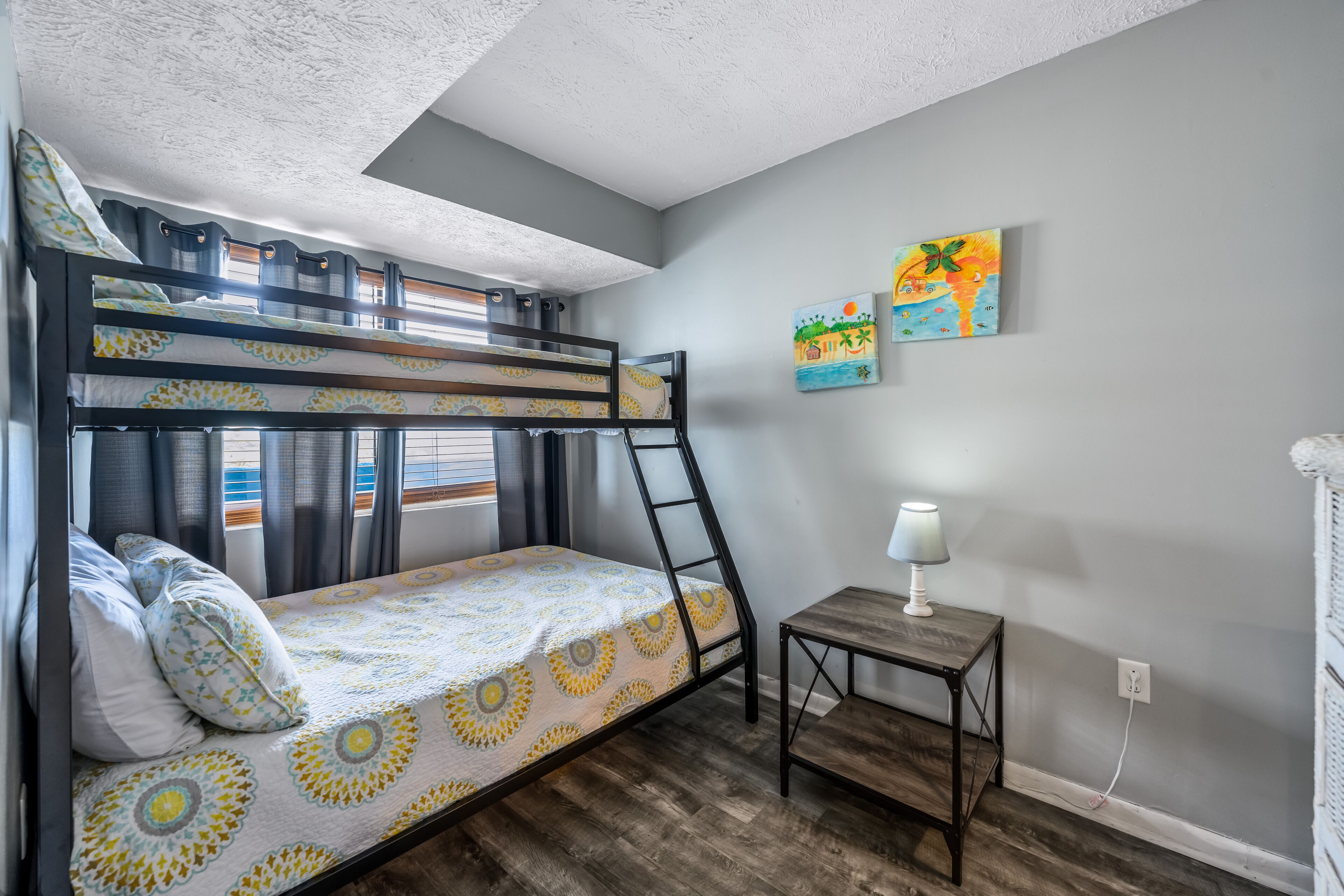 Une chambre avec un lit superposé, une échelle en bois, une petite table avec une lampe et deux tableaux accrochés au mur.