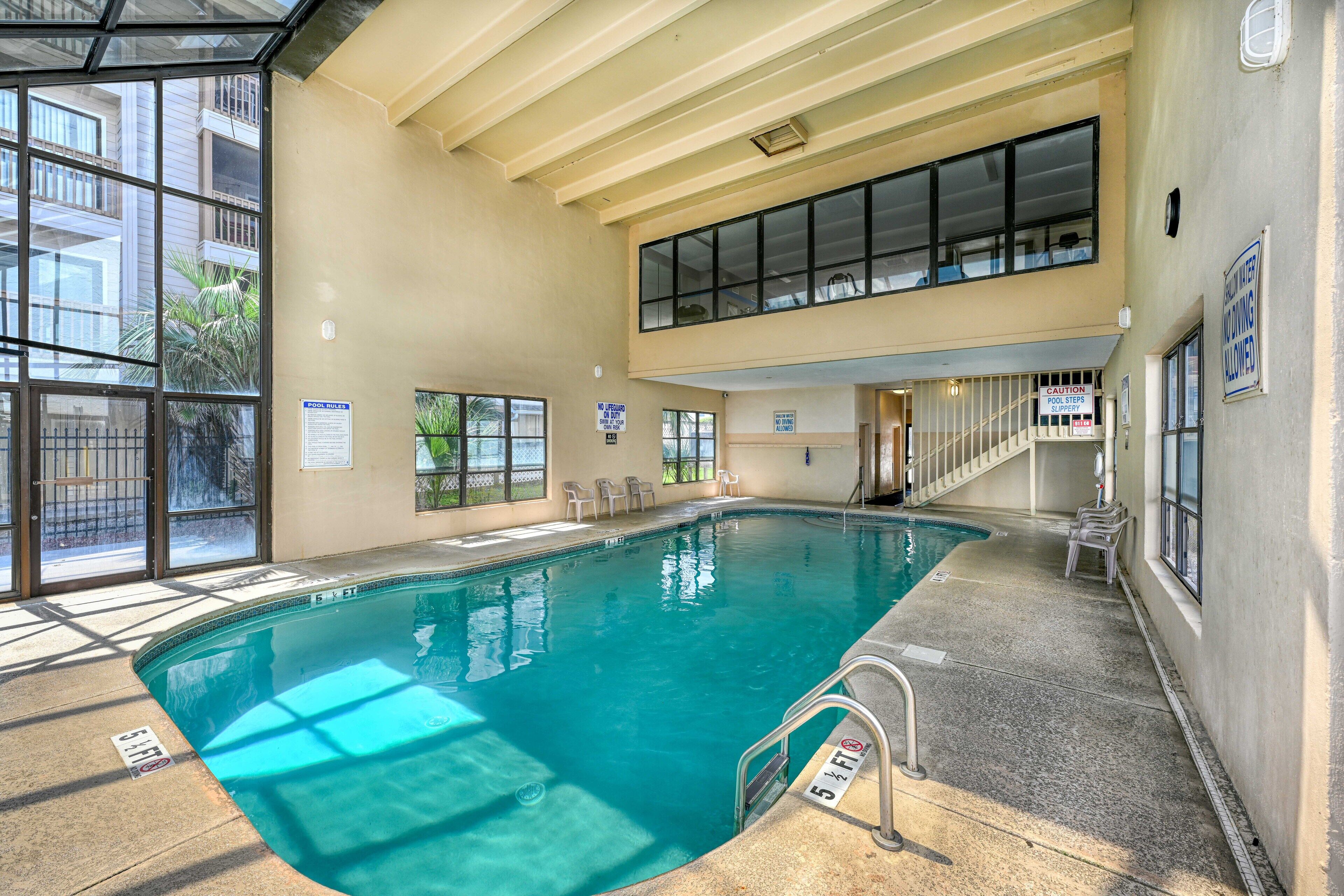 An indoor swimming pool with clear glass walls, a pool ladder, and a staircase leading to an upper level.