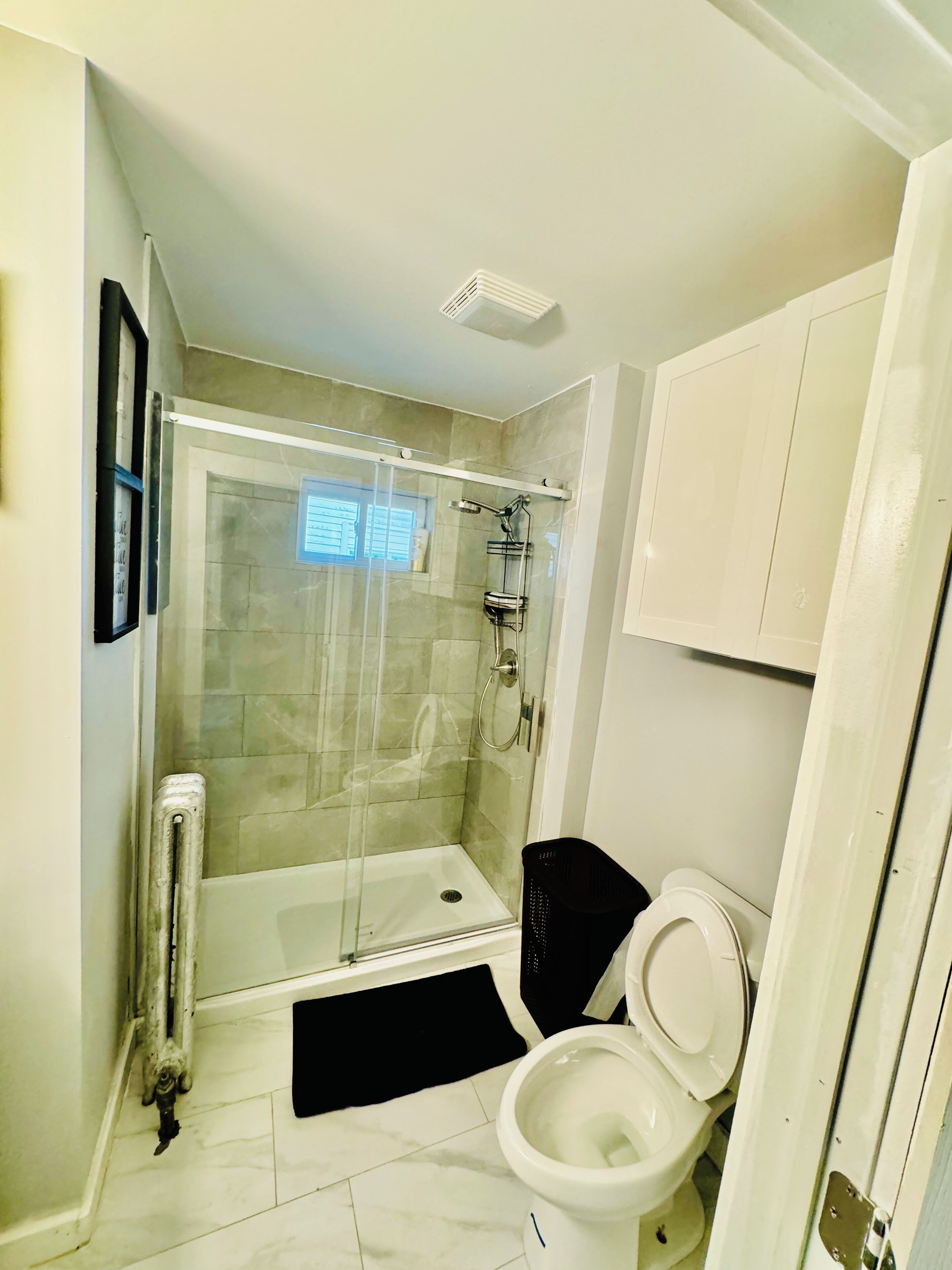A bathroom with a glass-enclosed shower, a white toilet, and a black mat on the floor.