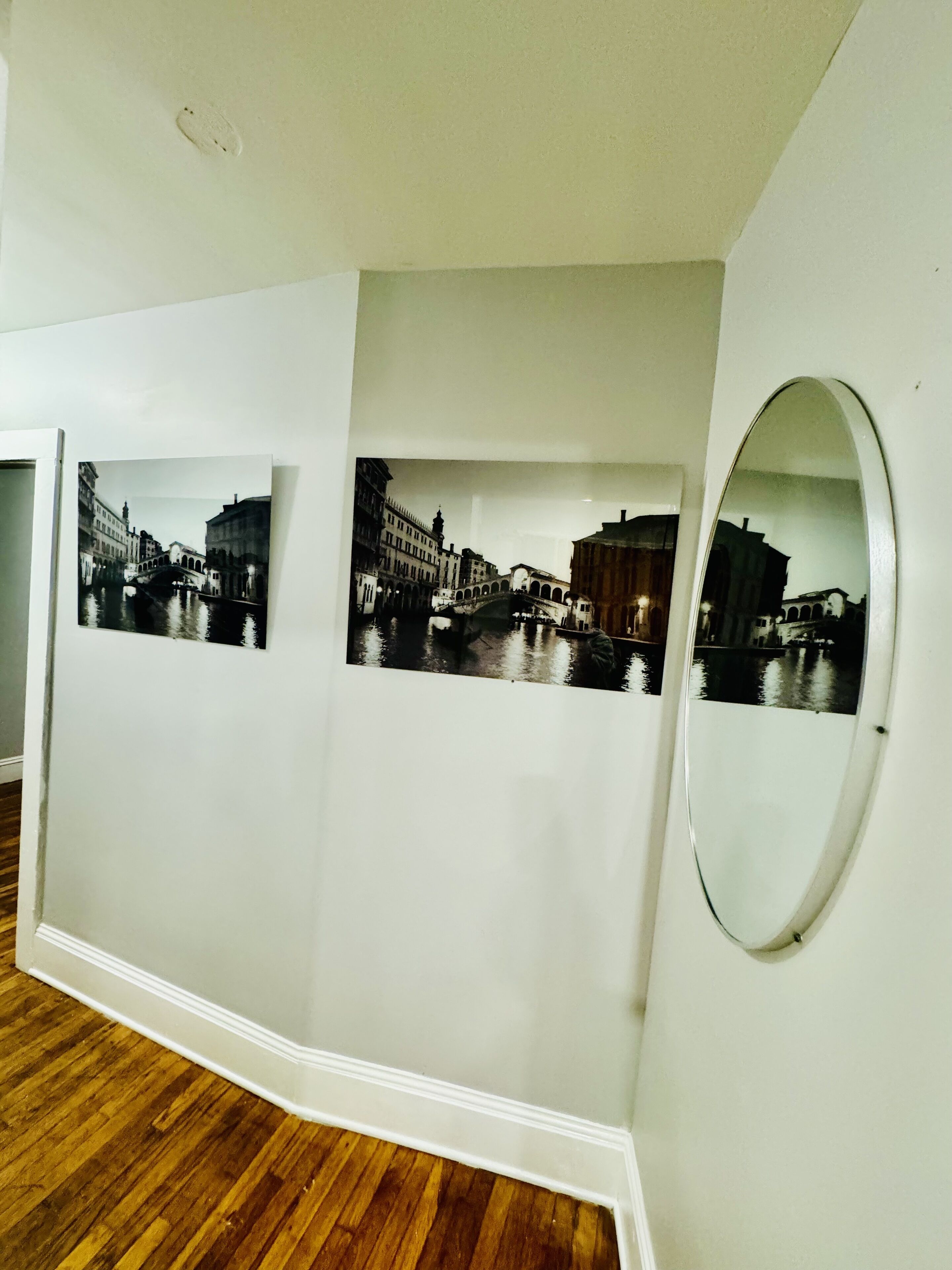Un couloir doté d’un plancher en bois, de murs blancs et de trois photographies en noir et blanc représentant une scène de canal.