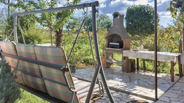 A patio with a swing chair, a stone table, and a pizza oven. - Holiday apartment with air conditioning (Valbandon)