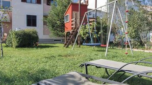 A grassy yard with a swing set, a small red playhouse, and a poolside area with lounge chairs. - Holiday apartment with air conditioning (Valbandon)