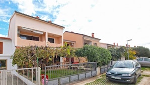 A residential area with a row of houses, a car parked in front, and a paved driveway. - Holiday apartment with air conditioning (Valbandon)