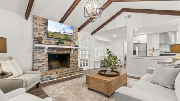 Una sala de estar con chimenea de piedra, un televisor montado arriba y una cocina al fondo.