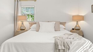 Un dormitorio con cama, dos mesitas de noche con lámparas, una ventana con cortinas y vistas al exterior.