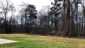 An open grassy area with a concrete slab, surrounded by trees. - Brand NEW Entire home in Statesville, NC (Statesville)