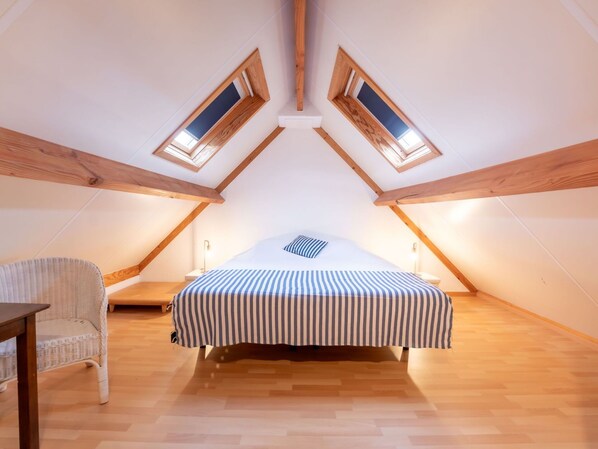A small, cozy attic bedroom with a bed, a chair, and two skylights.