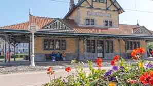 Una estació de tren històrica amb un andró cobert i un edifici amb la inscripció "De Baan Aan Zee".