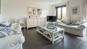 Un saló modern amb un sofà blanc, una taula de centre de vidre amb llibres, un televisor i un moble blanc amb un mirall.