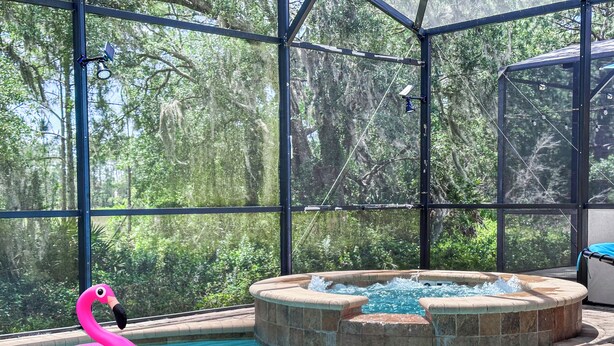 An indoor swimming pool with a hot tub, surrounded by a glass enclosure with a view of trees.