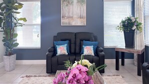 A living room with a dark blue wall, a black sofa with starfish pillows, a framed painting, and a potted plant.