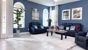 A living room with a dark blue wall, two black leather sofas, a coffee table, and a ceiling fan.