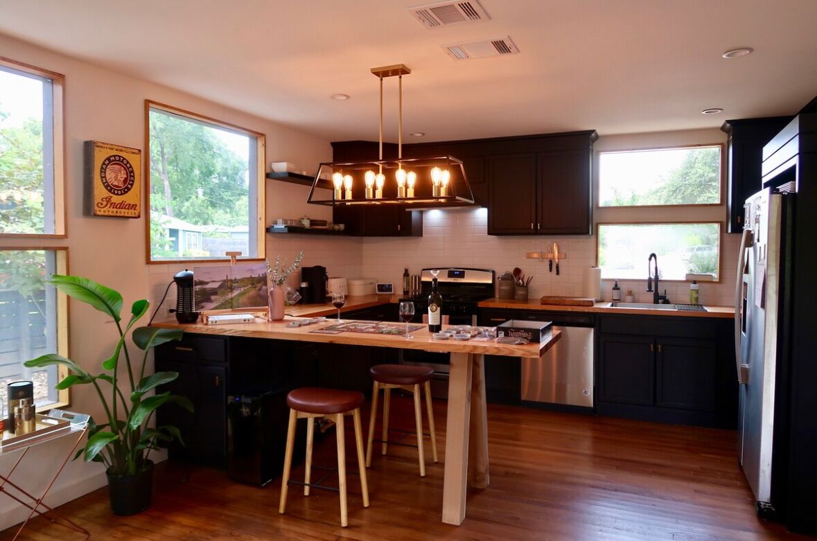 A modern kitchen with a wooden island, bar stools, and a pendant light.