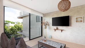 A modern living room with a sofa, a coffee table, a TV mounted on the wall, and a large sliding glass door leading to an outdoor balcony.