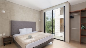A modern bedroom with a large bed, a wardrobe, and a balcony with a view of trees.