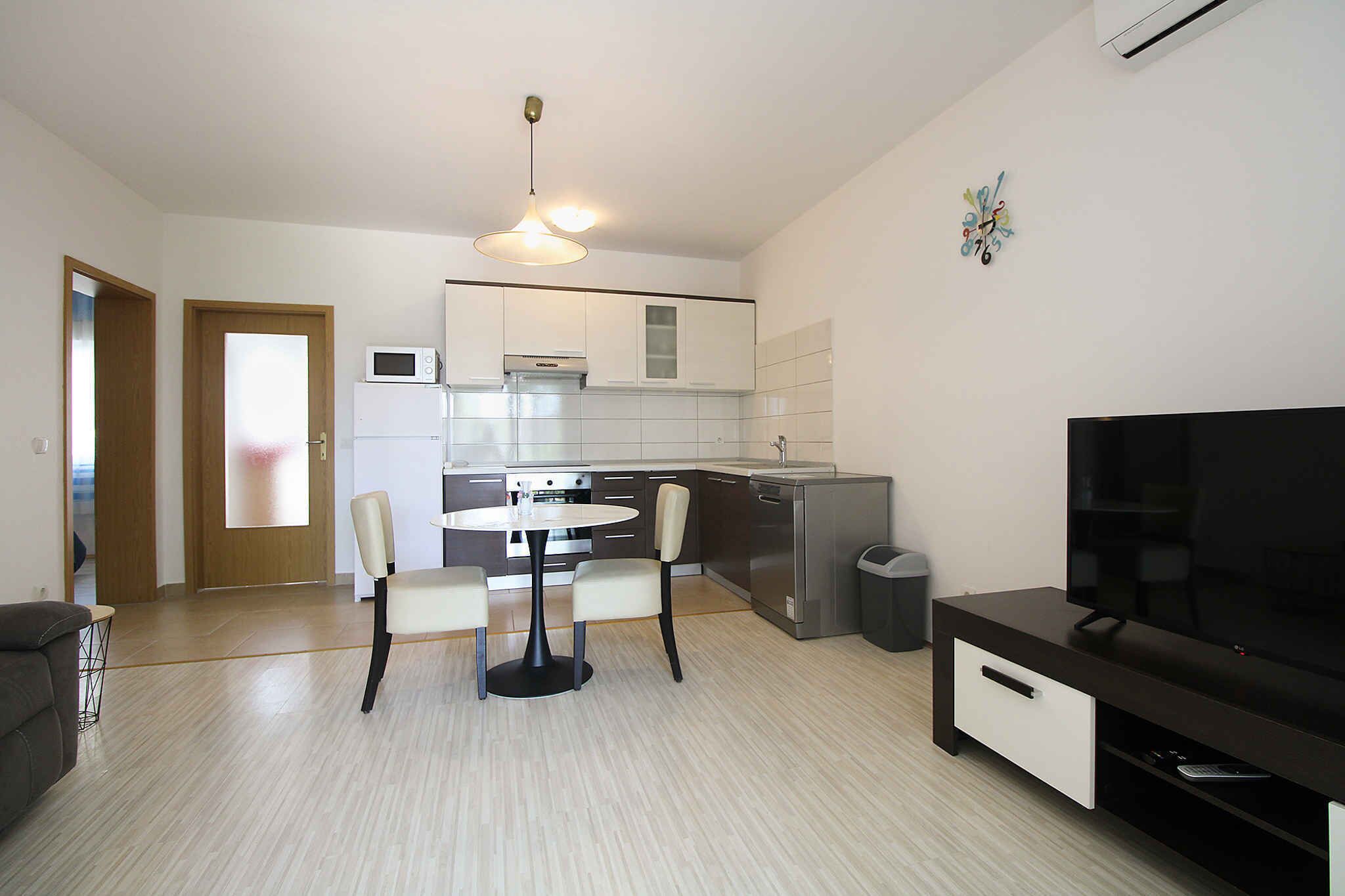 A modern kitchen with a dining area, a TV, and a trash bin.