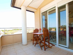 Un balcón con mesa y sillas, una puerta de vidrio que da al interior y vistas del entorno.