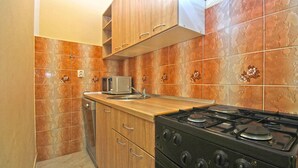 Une cuisine de taille réduite, dotée de meubles en bois, d’une cuisinière à gaz, d’un four à micro-ondes et d’un évier.