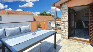 Une terrasse avec une table et des chaises, un pot de fleurs et une vue sur la rue.