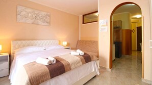 Une chambre d’hôtel avec un grand lit, une table de chevet, une œuvre d’art accrochée au mur et une porte donnant sur une autre pièce.