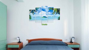 Een slaapkamer met een bed, twee nachtkastjes, een groene garderobe en een wanddecoratie bestaande uit meerdere panelen met een tropisch tafereel.