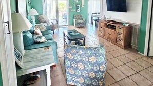Un salon spacieux aux couleurs turquoise, doté d’un téléviseur, d’un ventilateur de plafond et d’un coin repas avec une table et des chaises.