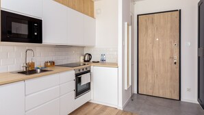 A modern kitchen with white cabinets, a wooden countertop, a microwave, a kettle, and a door with a wooden panel. - Nova Letnica Apartment (Gdansk)