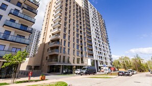 A high-rise residential building with multiple balconies, a covered entrance, and a parking area with several cars. - Nova Letnica Apartment (Gdansk)