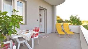 A balcony with a table and chairs, a door, and a view of greenery.