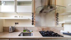 Una cocina moderna con un lavamanos de acero inoxidable, una estufa a gas y una campana extractora de vidrio.