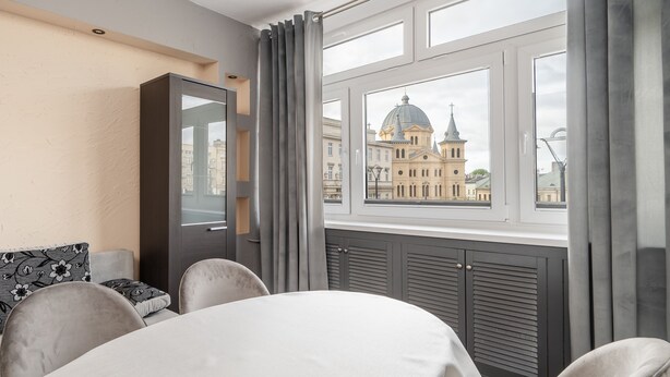 Una habitación con una mesa de comedor, sillas, un sofá y un ventanal con vistas a un edificio histórico.