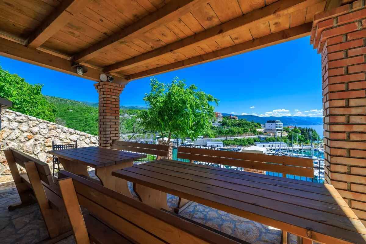 A wooden outdoor seating area with a view of a marina and hills in the background.