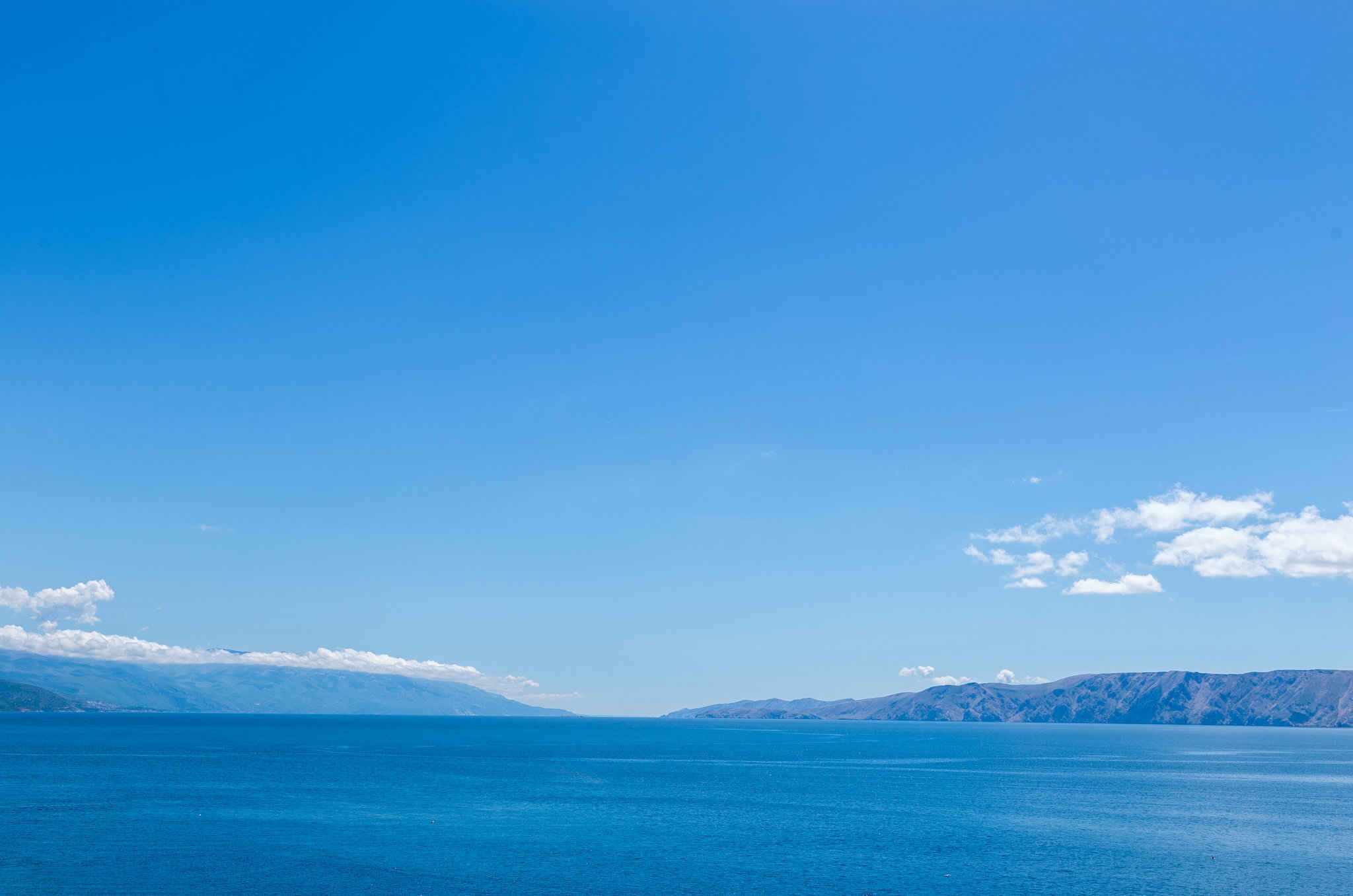 Une vue dégagée sur une mer calme et des montagnes lointaines, sous un ciel bleu.