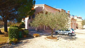 A building with a paved driveway, a parked car, and a tree in the foreground. - Holiday apartment with air conditioning (Fažana)