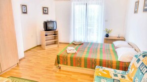 A bedroom with a bed, a television on a stand, a window with curtains, and a small table with a plant. - Holiday apartment with air conditioning (Fažana)