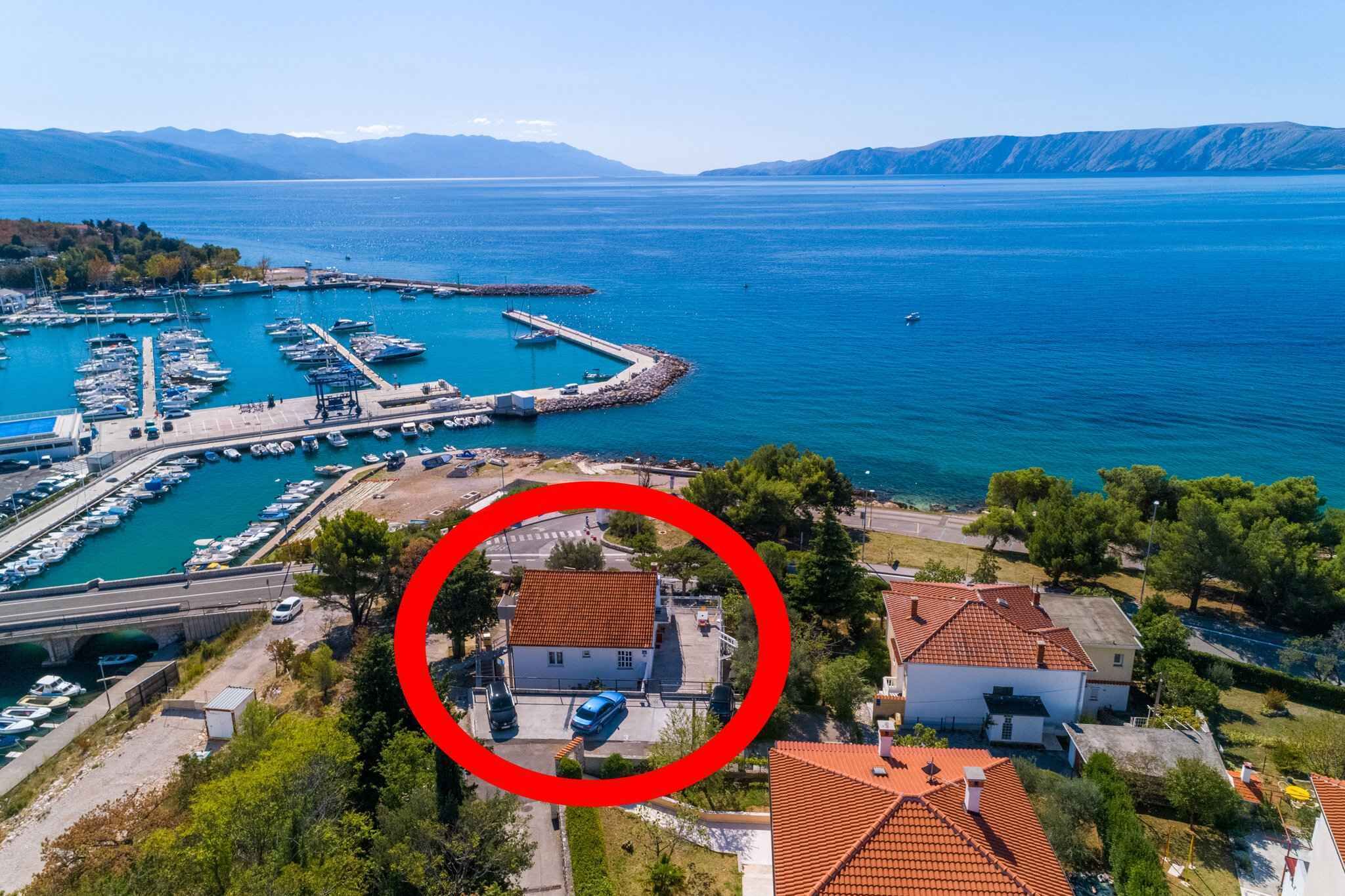 Un port de plaisance sur la côte, avec des bateaux, une petite maison avec un toit rouge et un pont au premier plan.