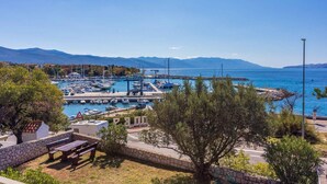 A marina with boats docked, a pier extending into the water, and mountains in the background.