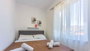 A hotel room with a bed, white curtains, and two wall art pieces.