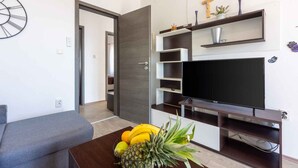 A modern living room with a grey sofa, a wooden coffee table with fruit, a flat-screen TV, and built-in shelves with decorative items.