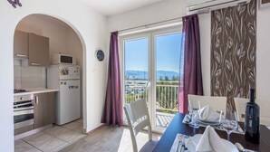 A compact kitchen with modern appliances, a dining area with a table set for two, and a balcony with a view of the sea.
