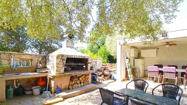 An outdoor kitchen with a stone oven, a dining table with chairs, and a patio area with a ceiling fan. - Studio with sea view and air conditioning (Peroj)