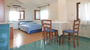 A bedroom with a bed, a small table with chairs, an air conditioning unit, and a window with curtains. - Studio with sea view and air conditioning (Peroj)