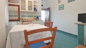 A dining area with a table and chairs, a kitchen in the background, and a television on a stand. - Studio with sea view and air conditioning (Peroj)